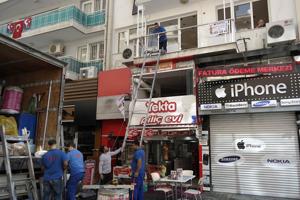 Dükkânların bulunduğu bir binanın üst katına kurulan eşya asansörü ve Güven-Tur ekibi