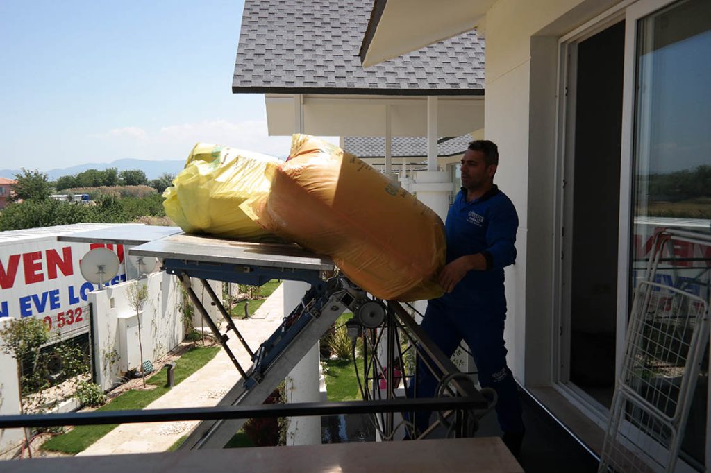 Güven-Tur çalışanı balkona ulaşan eşya asansörü platformundaki paketleri alıyor