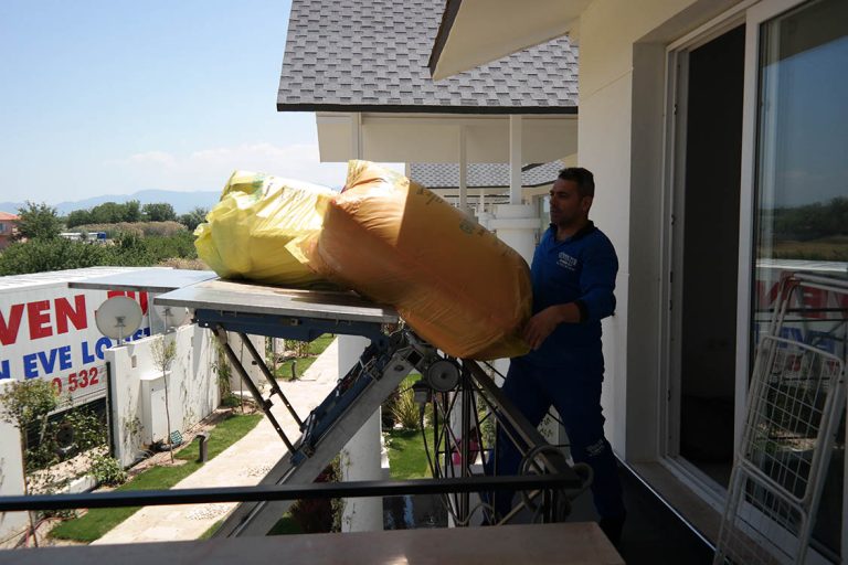 Güven-Tur çalışanı balkona ulaşan eşya asansörü platformundaki paketleri alıyor