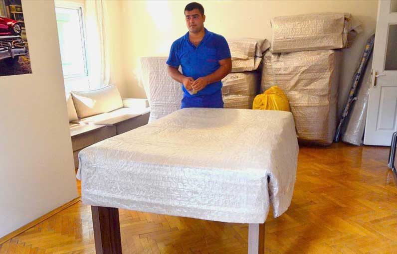 Güven-Tur çalışanı salondaki masayı koruyucu örtüyle paketliyor