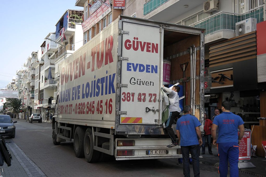 Güven-Tur kamyonu caddede yükleniyor, mavi iş kıyafetli ekip kasanın önünde